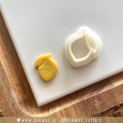 Cortador de massa em forma de limão junto a uma peça amarela cortada na mesma forma sobre superfície branca e tabuleiro de madeira