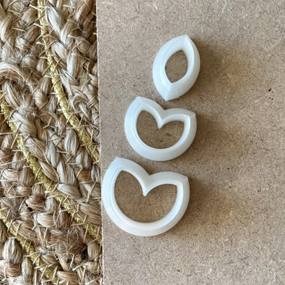 Conjunto de três cortadores de massa de plástico branco sobre superfície de madeira e tapete de fibras naturais