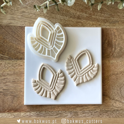 Cortadores e formas em silicone e argila formato folhas, com padrões geométricos, sobre placa branca em madeira.