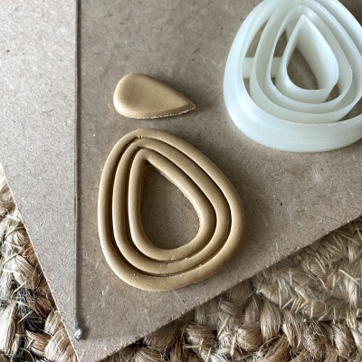 Cortadores de massa em silicone bege e branco em forma de gota sobre cartão e tecido trançado