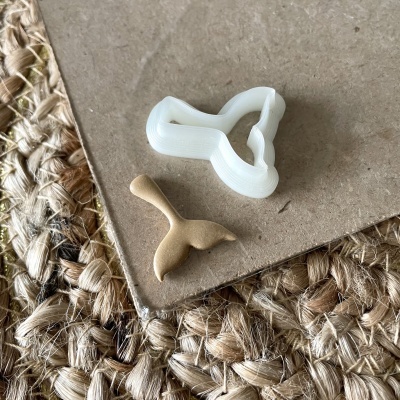 Cortador de bolacha branco em forma de cauda de baleia com massa castanha e superfície de cortiça e tapete rústico