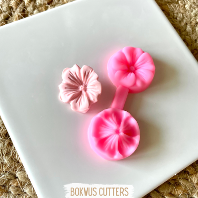 Dois cortadores de flores cor-de-rosa em plástico sobre prato branco e fundo de juta.