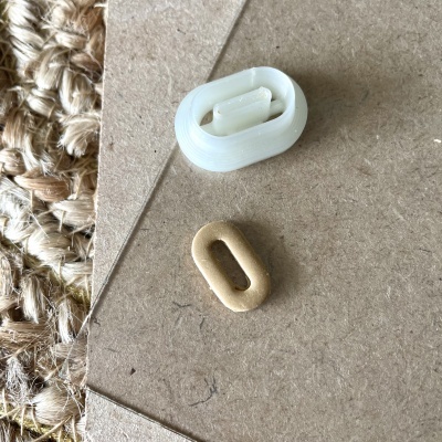 Duas ilhóses, uma branca e outra dourada, sobre papelão castanho com tapete ao lado