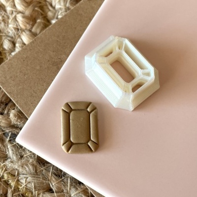 Peça retangular bege com padrão facetado ao lado de molde branco sobre superfícies diversas.