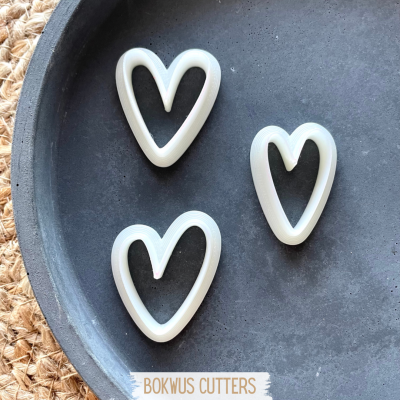 Três cortadores de biscoito em forma de coração brancos num prato escuro sobre superfície de corda