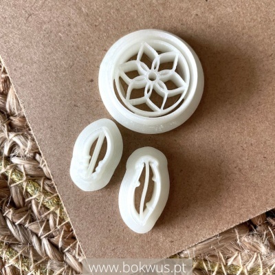 Três cortadores de massa brancos com formas decorativas em cima de superfícies castanhas e trançadas.