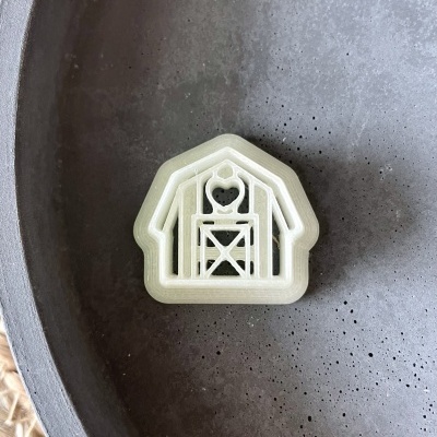 Cookie cutter plástico branco celebrando um celeiro em prato cinza texturizado