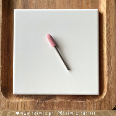 Broca rotativa com ponta rosa sobre azulejo branco em base de madeira