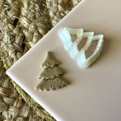 Moldes para biscoitos em forma de árvore de Natal e biscoito dourado sobre base rosa com fundo de tapete de fibra natural