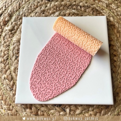 Rolo texturizador para bolo rosa e amarelo com padrão de espirais numa superfície branca