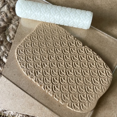 Rolo de textura branco sobre massa castanha com padrão estampado repetitivo em superfície de cartão