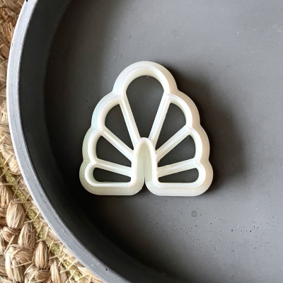 Cortador de massa branco em formato de leque dentro de um prato cinza sobre superfície de tecido natural