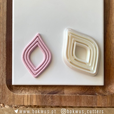 Cortantes plásticos em forma de losango e massa rosa cortada sobre base branca e tabuleiro de madeira