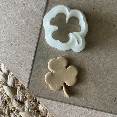 Cortador de massa branco e massa em forma de trevo sobre superfície de vidro