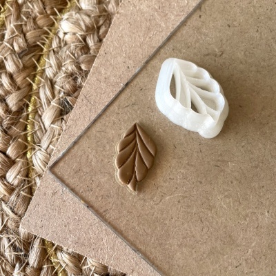 Carimbo de folha branco e peça carimbada em argila marrom sobre madeira e tecido rústico