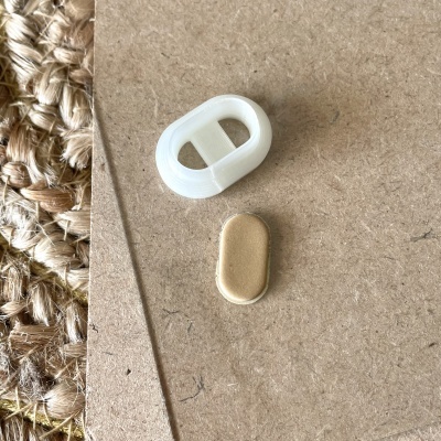 Objeto dourado oval e peça plástica branca sobre madeira e tapete de fibras