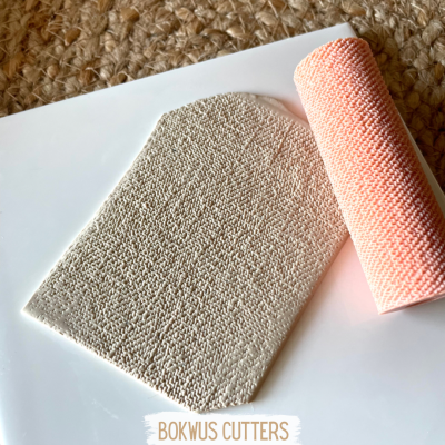 Pano de microfibra cinzento e rolo de pano laranja sobre placa branca com texto BOKWUS CUTTERS