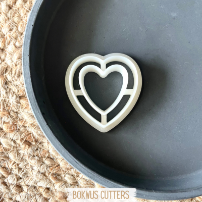 Cortante de bolacha coração branco numa panela preta sobre superficie de corda.