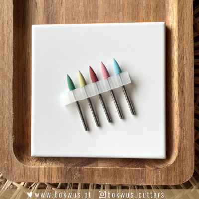 Conjunto colorido de cinco pontas esmeriladas com base metálica sobre azulejo branco e tabuleiro de madeira