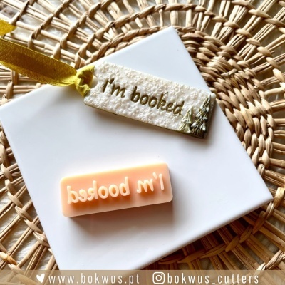 Carimbo de borracha cor-de-rosa e etiqueta branca com texto 'I'm booked' sobre fundo de tecido trançado