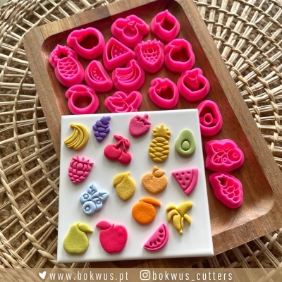 Cortadores de silicone rosas em forma de frutas com moldes coloridos em suporte branco e tabuleiro de madeira.