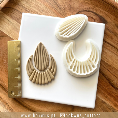 Cortadores de massa ou argila brancos com padrão geométrico e régua dourada sobre fundo branco e madeira.