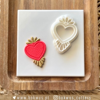 Molde de corte branco com formato de coração e corte vermelho e dourado sobre placa branca e base de madeira