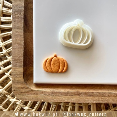 Duas formas de abóbora, branco e laranja, em prato branco sobre base de madeira e tapete de fibras