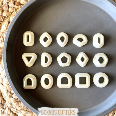 Conjunto de cortadores de massa creme em formas geométricas num prato cinza escuro sobre superfície de palha trançada.