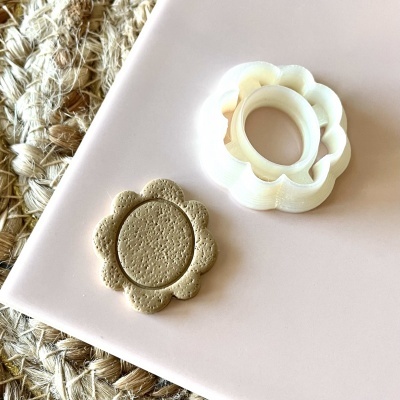 Cortador de biscoitos branco em forma de flor com biscoito em cima de base cor de rosa e ráfia ao lado.