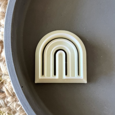 Pendente ou broche bege em forma de arco-íris sobre superfície cinzenta