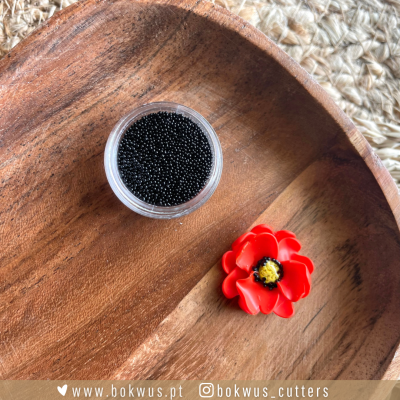 Microesferas pretas num recipiente com flor vermelha decorativa numa bandeja de madeira.