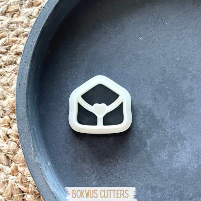 Cortador de bolachas branco em forma de envelope com coração sobre prato preto e tapete de fibras naturais