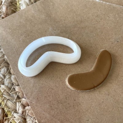 Dois acessórios de cabelo em forma curva, um branco e outro castanho, sobre mesa de madeira clara