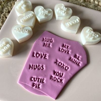 Carimbos brancos em forma de coração e matriz rosa com frases gravadas em relevo.