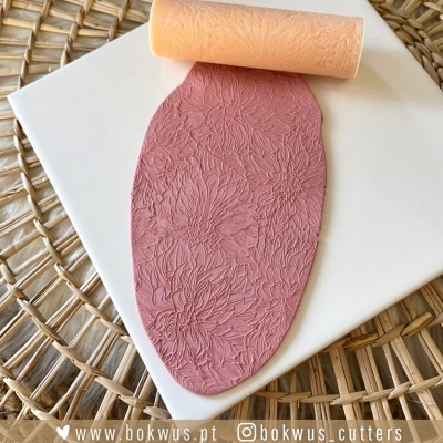 Rolo de textura floral cor de pêssego e pasta de modelar rosa sobre base branca em tapete de fibras naturelles