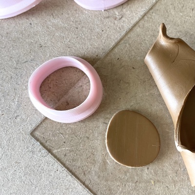 anel rosa claro, objeto dourado e sapato dourado sobre superfície de pedra