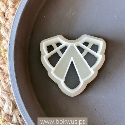 Cortador de biscoitos branco em forma decorativa dentro de tigela cinza sobre superfície trançada