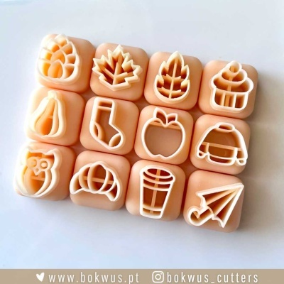 Doze cortadores de biscoitos quadrados cor salmão com desenhos variados em branco, sobre fundo branco.