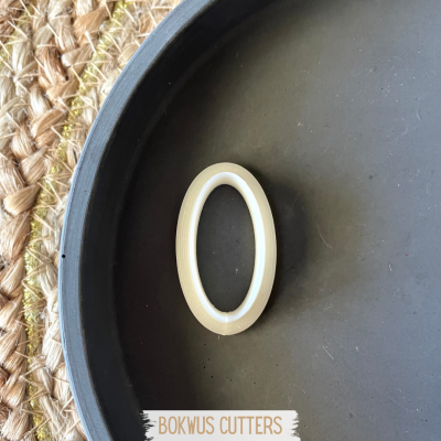 Anel oval bege com textura, sobre prato preto em superfície de palha entrelaçada