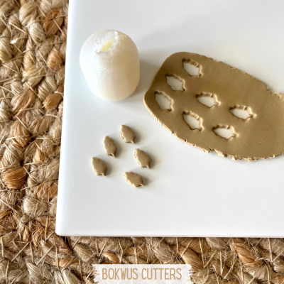 Carimbo cortador em argila com recortes de folhas e vela branca sobre base branca com tapete de fibras naturais