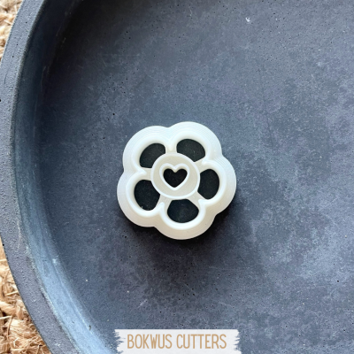 Cortador de massa em forma de flor branca com coração no centro sobre fundo escuro