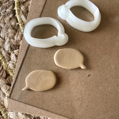 Dois cortadores de plástico branco e duas peças de polímero bege sobre cartão e tapete de fibras naturais