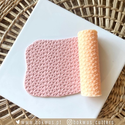 Rolo de silicone texturizado cor pêssego sobre superfície plana branca com padrão em rosa claro