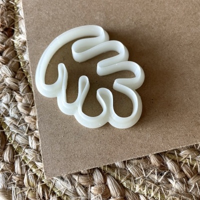 Cortador de bolachas branco em forma de folha sobre cartão e tapete natural