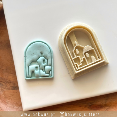 Dois cortadores de pastelaria em formato de casas, um azul turquesa e outro bege, sobre superfície branca