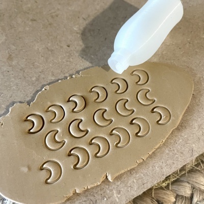 Material de modelagem castanho com padrão de luas crescentes e ferramenta branca sobre superfície cinzenta.