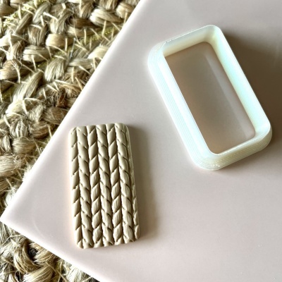 Molde branco retangular e peça moldada bege com padrão de trança sobre superfície rosa claro e tapete de fibras naturais