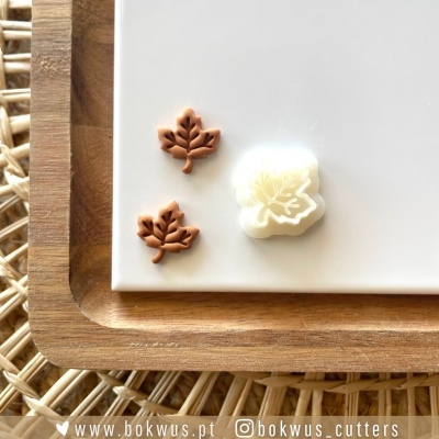 Molde cortador de folha em silicone branco com duas peças castanhas em forma de folha numa placa branca e base de madeira.