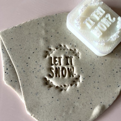 Selante branco com letras em relevo Let It Snow usado para marcar massa cinzenta com pedaços pretos